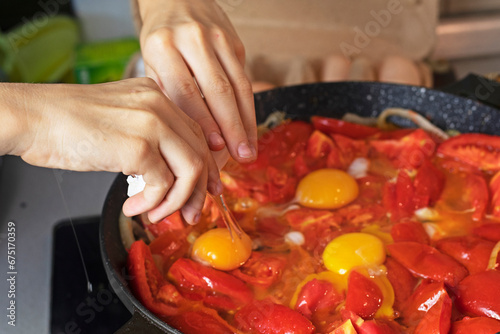 crack an egg into a frying pan with tomatoes © Nataliia Makarovska