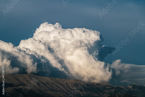 Huge cumulus cloud on top of mountain against dramatic moody sky, landscape
