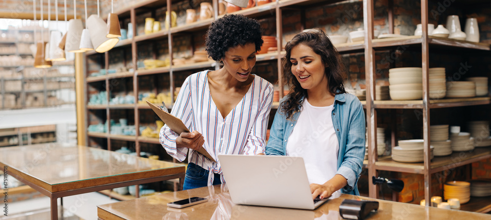 Two young shop owners using a laptop in their store - obrazy, fototapety, plakaty 