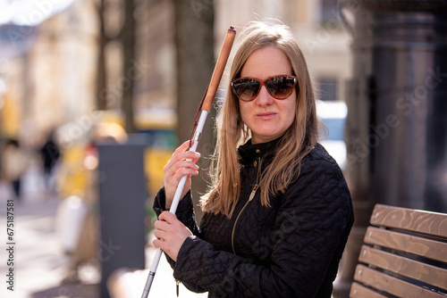A visually impaired woman holding a white cane and sitting on a bench in the city