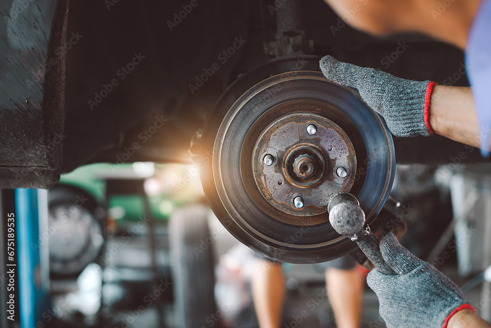 Auto mechanics in the garage replace brakes. A mechanic installing a car wheel while doing maintenance. A laborer changing the brake disk. Idea for putting in a brake disk. - obrazy, fototapety, plakaty 
