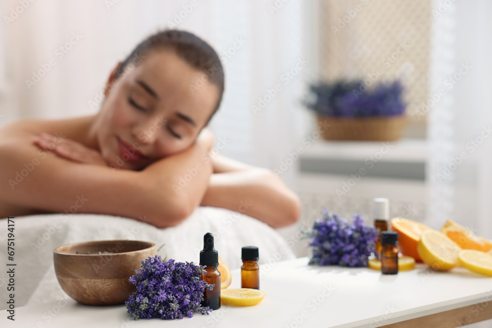 Woman relaxing on massage couch and bottles of essential oil with ingredients on table in spa salon, selective focus - obrazy, fototapety, plakaty 