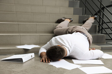 Unconscious man with scattered folder and papers lying on floor after falling down stairs indoors