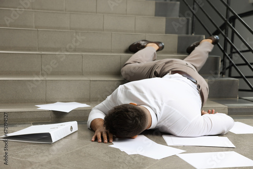 Unconscious man with scattered folder and papers lying on floor after falling down stairs indoors photo