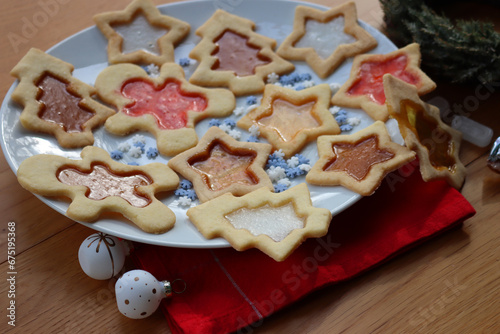 Christmas cookies with fake “glass” made of melted candies on plate on wooden table with festive decorations