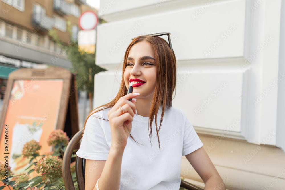 Happy beautiful woman with a smile in a white fashionable T-shirt sits in a cafe on the street and smokes a modern e cigarette. Pretty girl enjoy Happy beautiful woman with a smile in a white fashionable T-shirt sits in a cafe on the street and smokes a modern e cigarette. Pretty girl enjoy