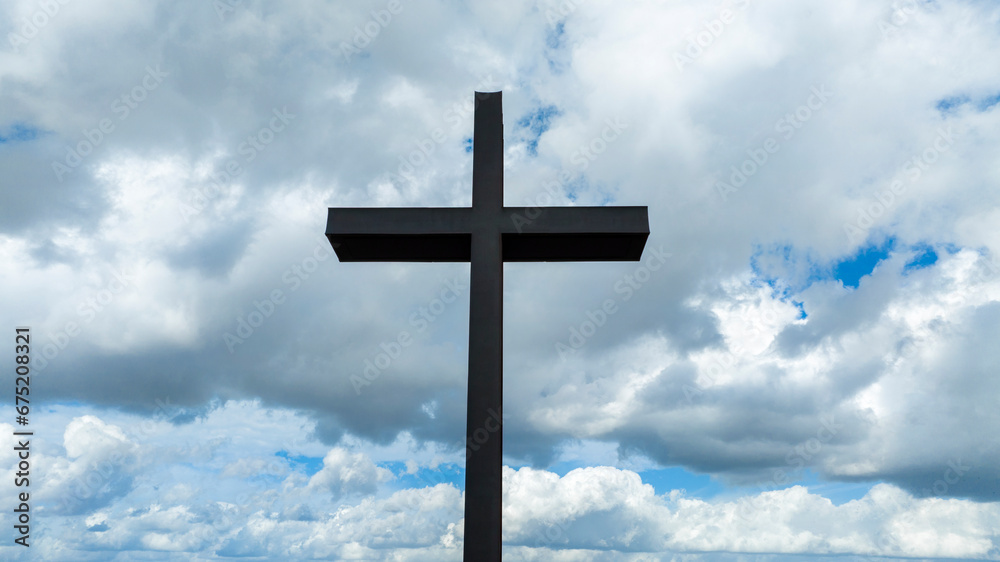 Closeup of a metal sculpture of a Christian cross. In the background the blue sky with some clouds creates a mystical atmosphere.