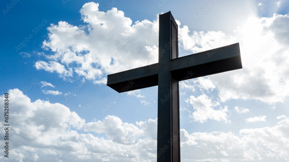 Closeup of a metal sculpture of a Christian cross. In the background the blue sky with some clouds creates a mystical atmosphere. Closeup of a metal sculpture of a Christian cross. In the background the blue sky with some clouds creates a mystical atmosphere.