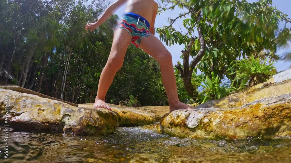 A boy in swimming trunks steps over a mountain stream of clear water A boy in swimming trunks steps over a mountain stream of clear water