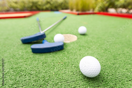 Assorted miniature golf putters and balls askew on synthetic grass.