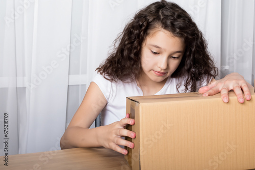 the girl opens the box. a girl sits on the sofa in the room and opens a box from online delivery. delivery of parcels from online stores concept