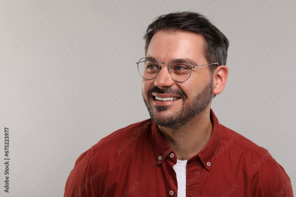 Obraz premium Portrait of happy man in stylish glasses on light grey background. Space for text