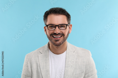 Portrait of happy man in stylish glasses on light blue background © New Africa