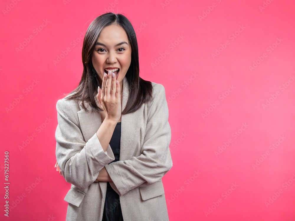 A portrait of an Indonesian Asian woman wearing a cream-colored blazer, posing in surprise and covering her mouth. Isolated against a magenta background. A portrait of an Indonesian Asian woman wearing a cream-colored blazer, posing in surprise and covering her mouth. Isolated against a magenta background.