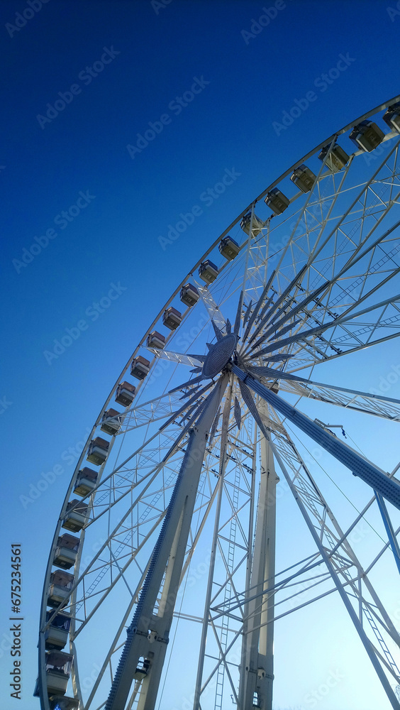 Upward view of a majestic Ferris wheel against a clear blue sky, symbolizing joy and leisure in a modern urban setting.