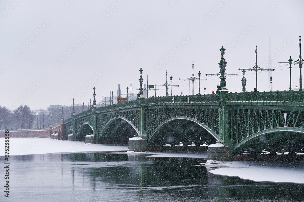 Naklejka premium An ancient beautiful bridge over the river in winter. It's snowing over the city.
