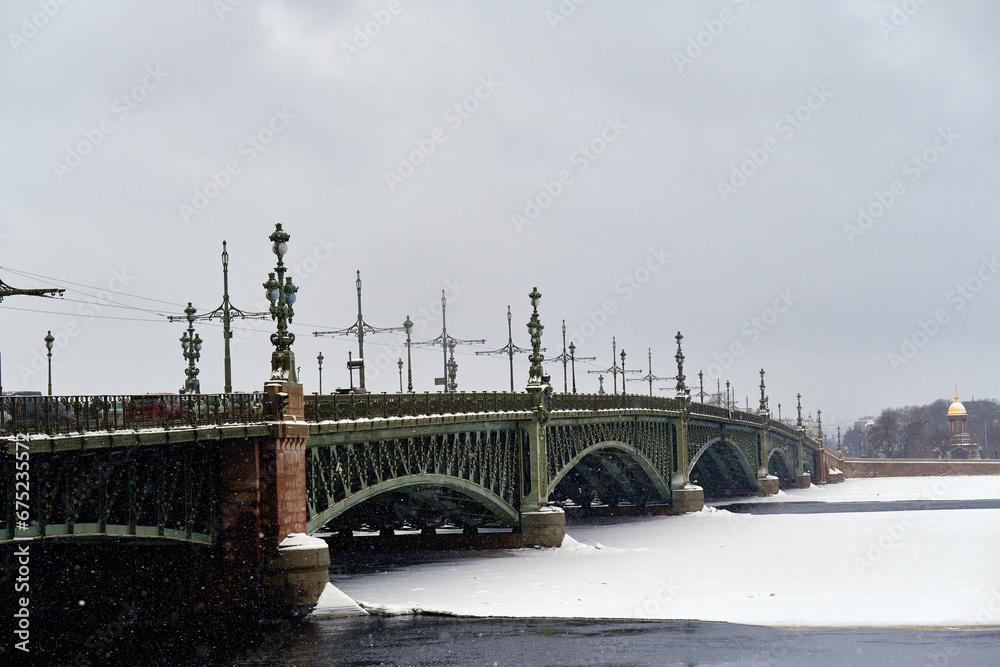 An ancient beautiful bridge over a frozen river in winter. Cityscape, it's snowing outside. Cold snowy winter.