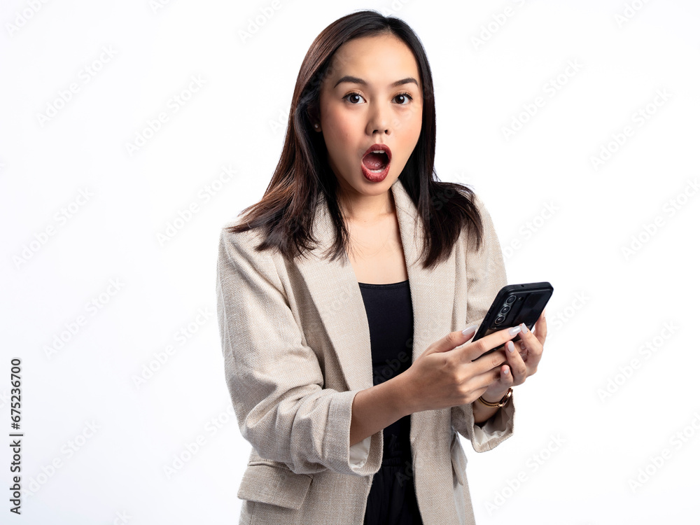 A portrait of an Indonesian Asian woman wearing a cream-colored blazer, looking happy while responding to a text message. Isolated against a white background. A portrait of an Indonesian Asian woman wearing a cream-colored blazer, looking happy while responding to a text message. Isolated against a white background.