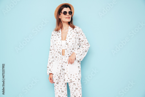 Young beautiful smiling female in trendy summer costume clothes. Carefree woman posing near blue wall in studio. Positive model having fun indoors. Cheerful and happy. In hat, sunglasses © halayalex