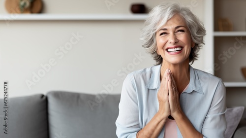 a cheerful older woman sits on her cozy home couch, smiling with her perfect white teeth and laughing with a hand-on-chest gesture, enjoying leisure and having a great time