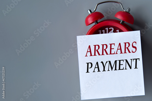 ARREARS PAYMENT - words on a white piece of paper on a gray background. Red alarm clock with white piece of paper
