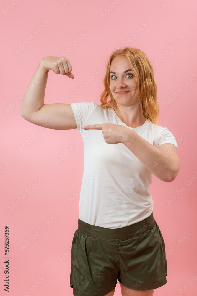 Green Eyes young woman showing muscles . Side view portrait lovely powerful cheerful red hair gerl on pink pastel background Green Eyes young woman showing muscles . Side view portrait lovely powerful cheerful red hair gerl on pink pastel background