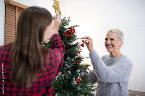 Family winter holiday and concept happy senior woman with adult daughter decorate christmas tree at home