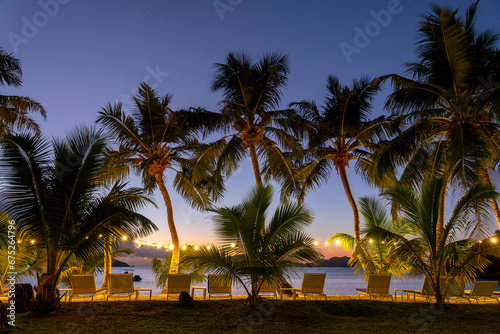 Illuminated palm trees and lounge chairs at night in Praslin island, Seychelles © Delphotostock