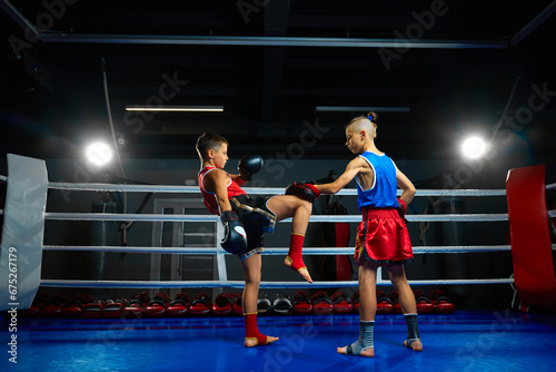 Two serious boys, kids, kickboxers, professional martial arts sportsmen performing kicks, practicing punches on punching pad.