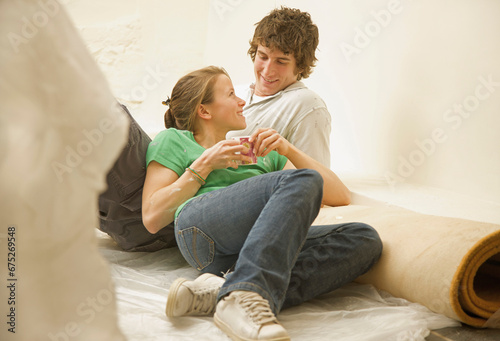 Couple having a break from DIY lying on the floor leaning on a rolled up carpet and looking at each 
