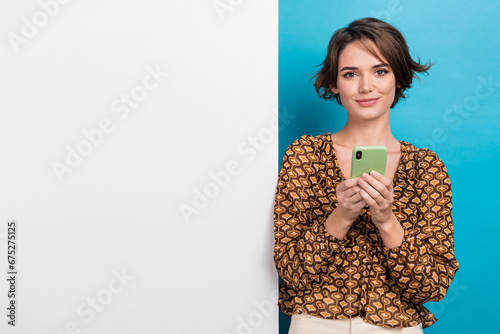 Photo of cute positive girl use smart phone chatting empty space billboard isolated on blue color background photo