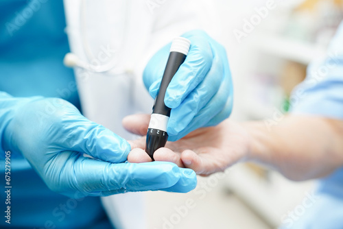 Asian doctor using lancet pen on senior patient finger for check sample blood sugar level to treatment diabetes.