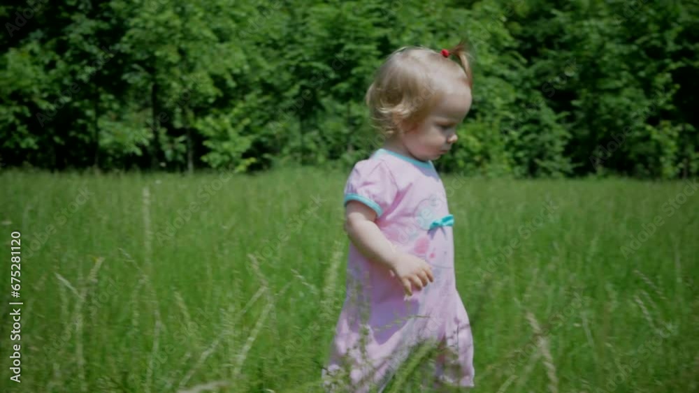 The baby learns to take the first steps. A cute little girl is learning to walk on a blade of grass. The baby laughs happily. A happy family.