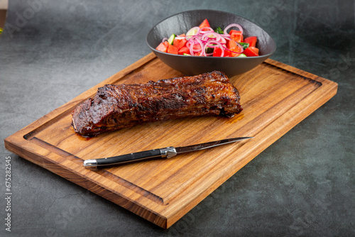 well-done steak with tomato and cucumber salad on a wooden tray, side view