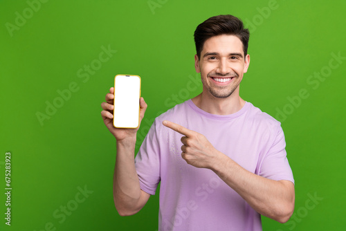 Photo portrait of attractive young guy hold device point white screen dressed stylish purple clothes isolated on green color background © deagreez