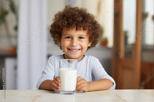 A handsome 4 year old smiling boy is sitting at the table with a glass of milk