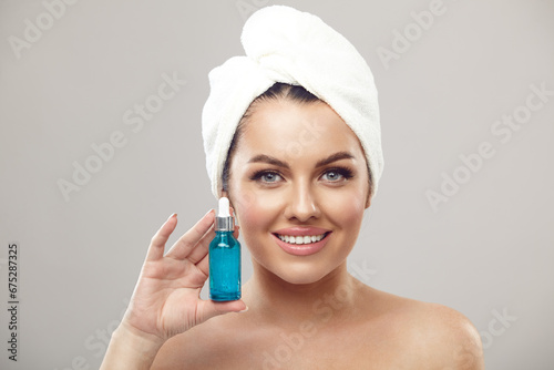 Happy young woman with beautiful skin demonstrates an effective serum for facial skin care on a grey isolated background.