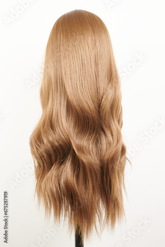 Natural looking dark blonde wig on white mannequin head. Long fair hair cut on the plastic wig holder isolated on white background