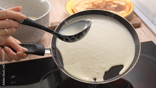 Pouring Batter onto Pan: A person's hand holds a ladle, guiding a smooth flow of batter onto a hot pan. Adjacent to this, a cooked crepe rests on a wooden board. Making pancake. Cooking food.  photo