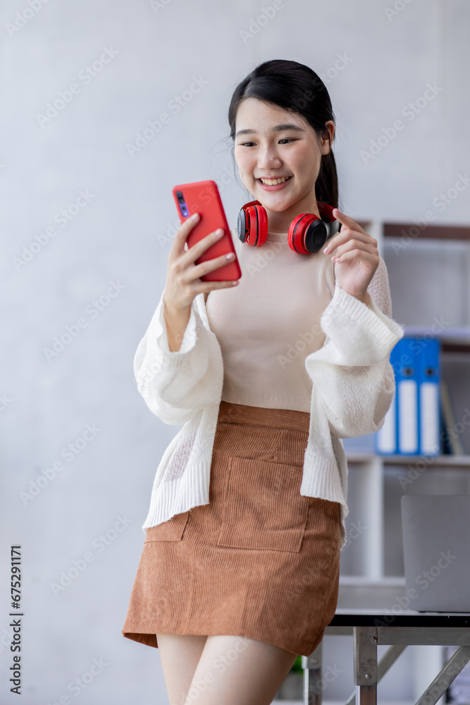 Happy young Asian woman using Phone sitting at desk, studying online, looking at phone screen learning web classes or having virtual call meeting remote working from home. Happy young Asian woman using Phone sitting at desk, studying online, looking at phone screen learning web classes or having virtual call meeting remote working from home.