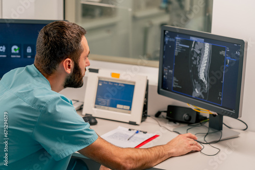 Concentrated male physician sits at a computer monitor in a room for describing MRI images and monitoring patient's condition