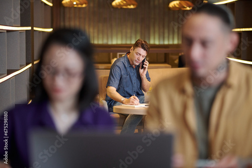 Middle-aged entrepreneur making phone call to business partner and writing down ideas photo