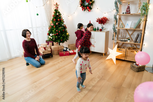 wide angle of smiling asian mother watching her young daughters having fun with balloons in a Christmas living room at home