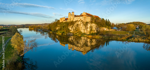 Tyniec near Krakow, Poland. Benedictine abbey and monastery on the rocky cliff and its water reflection in Vistula River. Aerial Panorama in autumn in sunset light
