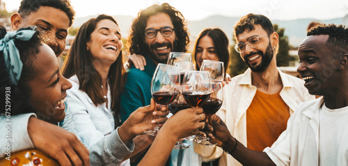 Young people toasting red wine glasses at farm house vineyard countryside - Happy friends enjoying happy hour at winery bar restaurant - Guys and girls having rooftop house party together photo