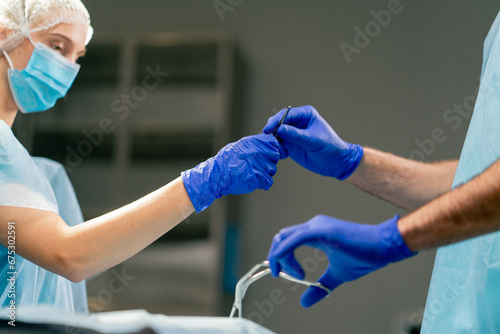 A girl assistant surgeon in uniform and a medical mask passes scalpel to her colleague during an operation