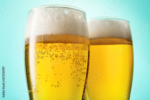 Two glasses with foamy beer on light blue background.
