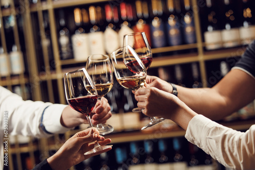 People in good mood clink glasses, celebrating together, photo focus on hands woman and man tasting degustation different types of wine, alcohol beverage to relax, bottles on shelves on background photo