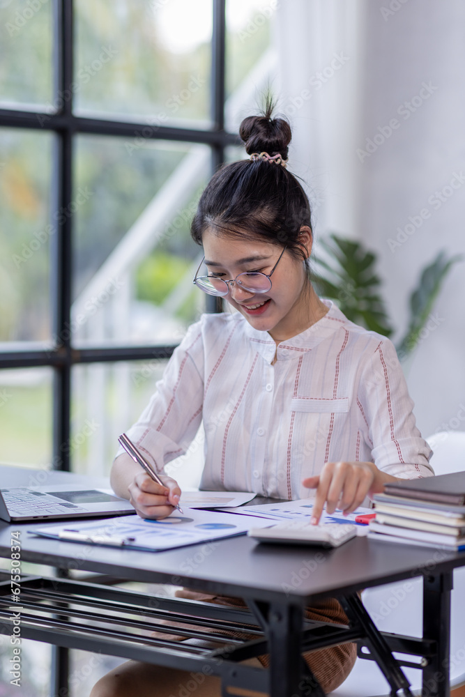 Young Asian Business woman Using laptop computer and working at office with calculator document on desk, doing planning analyzing financial report, business plan investment, finance analysis concept. Young Asian Business woman Using laptop computer and working at office with calculator document on desk, doing planning analyzing financial report, business plan investment, finance analysis concept.