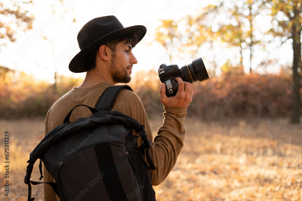 Nature photography concept. Professional nature photographer with digital camera and autumn forest on background - obrazy, fototapety, plakaty 